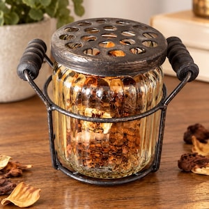 May include: A ribbed glass jar filled with dried potpourri, encased in a dark metal wire frame with two side handles and a matching dark metal lid featuring a grid of circular cutouts for ventilation and display.