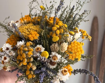 May include: A bouquet of dried flowers featuring vibrant yellow tansy clusters, white strawflowers with dark centers, and sprigs of purple lavender. The arrangement includes various green stems and thin, wispy foliage mixed throughout the floral display.
