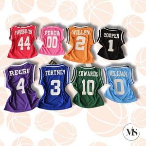 Puede incluir: Ocho camisetas de baloncesto en miniatura de diferentes colores con nombres y n&uacute;meros en la espalda. Las camisetas est&aacute;n dispuestas en dos filas de cuatro. Las camisetas son rosa, naranja, negro, rojo, morado, azul, verde y azul claro.