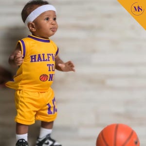 Puede incluir: Un ni&ntilde;o peque&ntilde;o vistiendo una camiseta de baloncesto amarilla y morada con el texto "Halfway to One" y un gr&aacute;fico de baloncesto. El ni&ntilde;o lleva una diadema blanca y sostiene un bal&oacute;n de baloncesto.