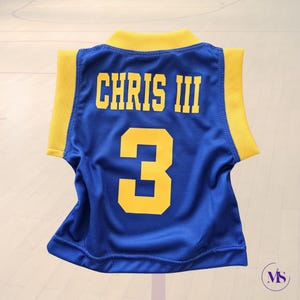 Puede incluir: Camiseta de baloncesto azul con ribetes amarillos y el nombre "CHRIS III" y el n&uacute;mero "3" en la espalda.