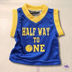 Puede incluir: Una camiseta de baloncesto azul y amarilla con el texto "HALF WAY TO ONE" y un gr&aacute;fico de baloncesto.