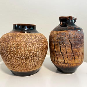 May include: Two ceramic vases with a crackled glaze finish. One vase is brown with a light brown crackled glaze, and the other is dark brown with a light brown crackled glaze.