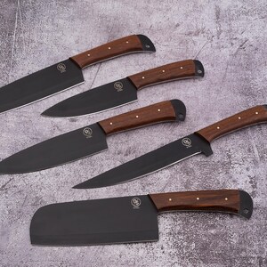 May include: Set of five black kitchen knives with wooden handles. The knives include a chef's knife, a paring knife, a bread knife, a utility knife, and a cleaver.