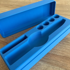May include: A blue plastic storage box with a lid. The box has a compartment for a watch and several smaller compartments for other items.
