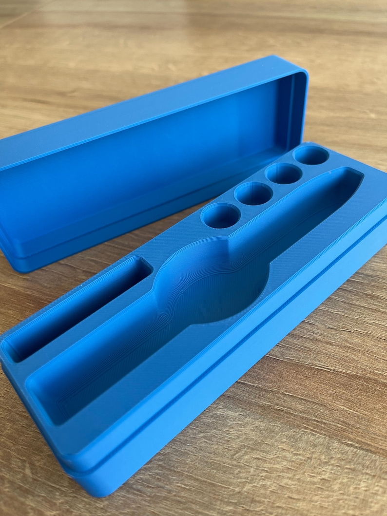May include: A blue plastic storage box with a lid. The box has a compartment for a watch and several smaller compartments for other items.