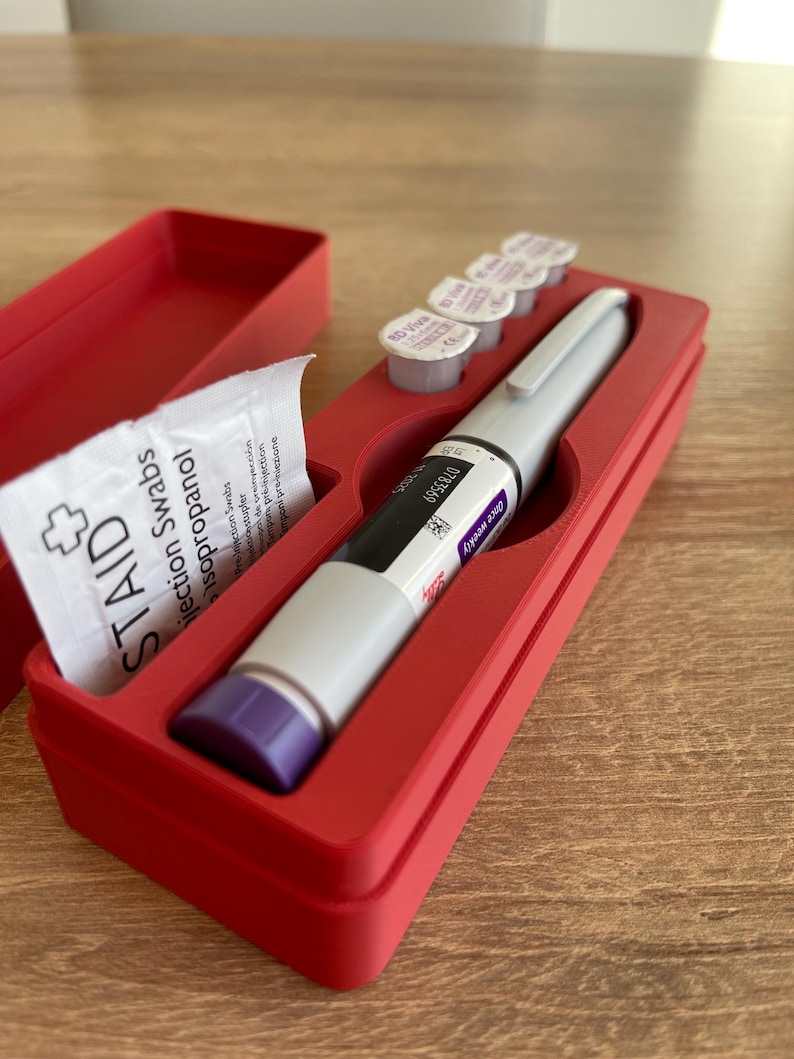 May include: A red plastic case with a compartment for a pen-like medical device, a small packet of alcohol swabs, and four small vials. The pen-like device has a purple cap and the text "Once weekly 0783569 3D Viva 1" printed on the side.