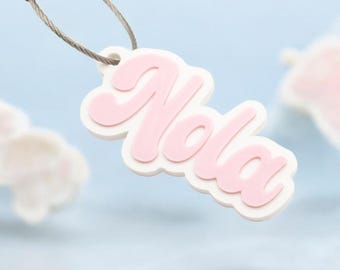 May include: A white keychain with a pink "Nola" name tag attached to a silver metal ring.