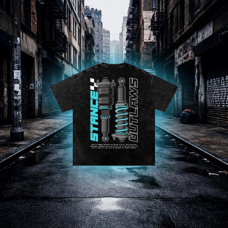 K&ouml;nnte beinhalten: Schwarzes T-Shirt mit einem grafischen Design von Automobil-Federungskomponenten. Die W&ouml;rter "STANCE" und "OUTLAWS" sind vertikal mit einer karierten Flagge dargestellt. Das Design ist in Blau und Wei&szlig; gehalten. Das T-Shirt hat einen Vintage-Look.