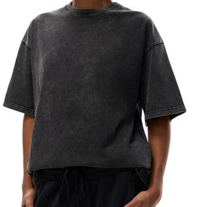 K&ouml;nnte beinhalten: Ein dunkelgraues T-Shirt mit S&auml;urewaschung und kurzen &Auml;rmeln. Das Shirt hat einen Rundhalsausschnitt und eine leicht &uuml;bergro&szlig;e Passform. Das Model tr&auml;gt eine schwarze Hose mit Kordelzug. Der Hintergrund ist wei&szlig;.