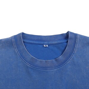 K&ouml;nnte beinhalten: Nahaufnahme eines blauen Rundhals-T-Shirts. Das Shirt hat einen gerippten Kragen und einen verblichenen, Vintage-Look. Das Etikett lautet "M". Der Stoff scheint eine weiche Baumwollmischung zu sein. Das Shirt ist einfarbig und hat einen l&auml;ssigen Stil.