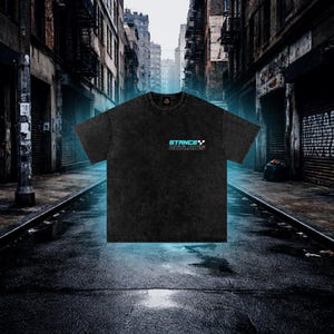 K&ouml;nnte beinhalten: Schwarzes T-Shirt mit dem Text "STANCE OUTLAWS" in Blau und Wei&szlig;. Das Shirt hat einen Rundhalsausschnitt und kurze &Auml;rmel. Das T-Shirt ist aus einem weichen, strukturierten Stoff gefertigt. Der Hintergrund ist eine Stadtstra&szlig;e.