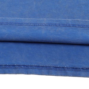 K&ouml;nnte beinhalten: Nahaufnahme eines Teils eines blauen Kleidungsst&uuml;cks, m&ouml;glicherweise ein T-Shirt oder &auml;hnliches. Der Stoff hat ein leicht verwaschenes Aussehen, mit sichtbaren N&auml;hten am Saum. Die Farbe ist ein kr&auml;ftiges, einfarbiges Blau.