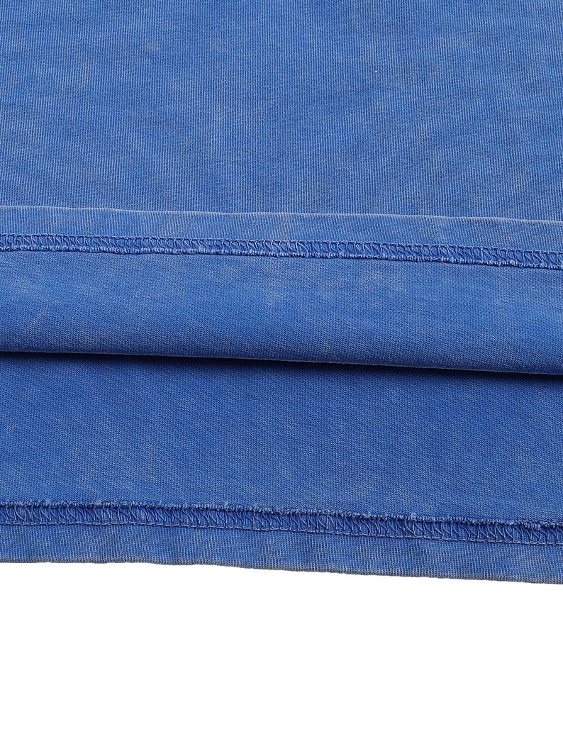 K&ouml;nnte beinhalten: Nahaufnahme eines Teils eines blauen Kleidungsst&uuml;cks, m&ouml;glicherweise ein T-Shirt oder &auml;hnliches. Der Stoff hat ein leicht verwaschenes Aussehen, mit sichtbaren N&auml;hten am Saum. Die Farbe ist ein kr&auml;ftiges, einfarbiges Blau.
