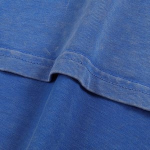 K&ouml;nnte beinhalten: Nahaufnahme eines leuchtend blauen Stoffes, m&ouml;glicherweise ein T-Shirt oder ein anderes Kleidungsst&uuml;ck. Die Textur des Materials ist sichtbar, mit subtilen Farbvariationen und einem markanten Nahtdetail. Der Stoff wirkt weich und leicht abgenutzt.