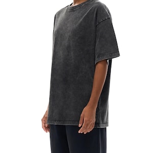 K&ouml;nnte beinhalten: Ein &uuml;bergro&szlig;es T-Shirt in Anthrazit mit Rundhalsausschnitt und kurzen &Auml;rmeln. Das Shirt hat ein verwaschenes, Vintage-Aussehen. Das Model tr&auml;gt auch eine dunkelblaue Hose.