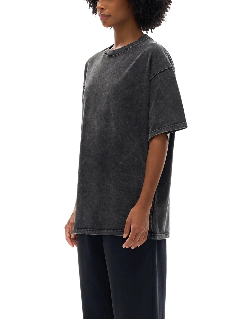 K&ouml;nnte beinhalten: Ein &uuml;bergro&szlig;es T-Shirt in Anthrazit mit Rundhalsausschnitt und kurzen &Auml;rmeln. Das Shirt hat ein verwaschenes, Vintage-Aussehen. Das Model tr&auml;gt auch eine dunkelblaue Hose.