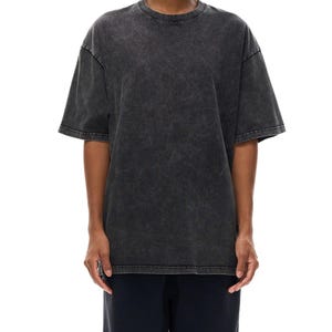 K&ouml;nnte beinhalten: Ein &uuml;bergro&szlig;es T-Shirt in Anthrazit mit Rundhalsausschnitt und kurzen &Auml;rmeln. Das Shirt hat ein verwaschenes, strukturiertes Aussehen. Das Model tr&auml;gt auch eine dunkelblaue Hose.
