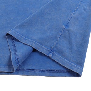 K&ouml;nnte beinhalten: Nahaufnahme eines blauen T-Shirts, das den Saum und einen Teil des &Auml;rmels zeigt. Der Stoff hat ein leicht verwaschenes Aussehen, mit sichtbaren N&auml;hten entlang der N&auml;hte. Die Farbe ist ein leuchtendes, mittleres Blau.