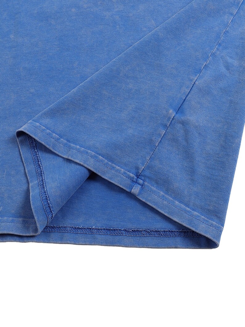 K&ouml;nnte beinhalten: Nahaufnahme eines blauen T-Shirts, das den Saum und einen Teil des &Auml;rmels zeigt. Der Stoff hat ein leicht verwaschenes Aussehen, mit sichtbaren N&auml;hten entlang der N&auml;hte. Die Farbe ist ein leuchtendes, mittleres Blau.