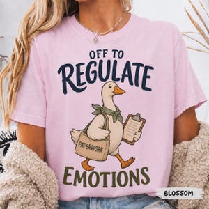 Puede incluir: Una camiseta rosa claro con el gráfico de un ganso que lleva un pañuelo verde, una bolsa de tela beige con la etiqueta "PAPERWORK" y sostiene un portapapeles. El texto "OFF TO REGULATE EMOTIONS" está impreso en letras azul oscuro y verde.