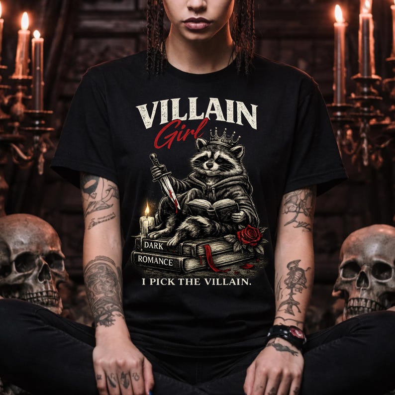 Dark romance Villain Girl I Pick The Villain shirt featuring gothic raccoon reading dark romance book with dagger candle and rose graphic on black Bella Canvas tee modeled by woman