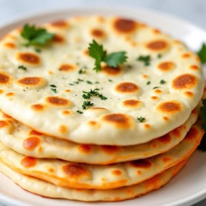 May include: A stack of four golden brown naan breads topped with fresh cilantro and a sprinkle of herbs.