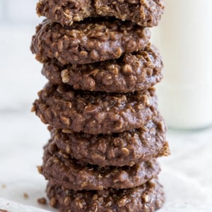 Puede incluir: Una pila de seis galletas de chocolate y avena, con una galleta ligeramente mordida en la parte superior. Las galletas son de color marrón oscuro y tienen una textura ligeramente crujiente.