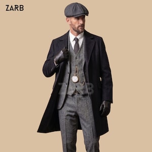 May include: A charcoal wool overcoat worn over a grey tweed three-piece suit with a white shirt and dark patterned tie. The outfit includes a grey flat cap, black leather gloves, and a gold pocket watch with a chain. The text ZARB is visible.