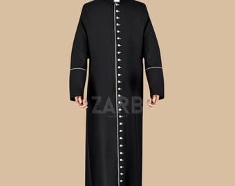 May include: Black clergy robe with white trim on the collar, cuffs, and down the front. The robe has a row of white buttons and the word "ZARB" is visible in the upper left and lower center. The robe is displayed on a mannequin.
