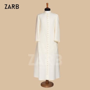 May include: A white, long-sleeved robe with a button-up front and a stand-up collar. The robe is on a wooden mannequin.
