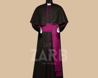May include: A black cassock with a pink sash and a matching cape. The cassock has a row of buttons down the front and a pink trim around the edges. The sash is tied at the waist and has a fringe at the bottom. The cape is attached at the shoulders and falls to the elbows. The text "ZARB TAILOR MADE" is printed on the bottom of the cassock.
