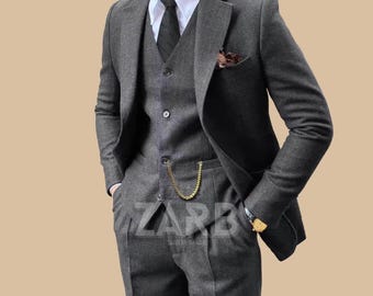May include: A three-piece grey suit with a matching waistcoat, jacket, and trousers. The suit includes a white shirt, black tie, and pocket square. The image displays the text "ZARB" in the upper left and lower center.