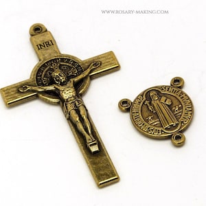 May include: A gold-toned metal crucifix with a depiction of Jesus Christ and the inscription "INRI" above his head. A separate gold-toned metal St. Benedict medal with the inscription "S. BENEDICTUS" around the edge.