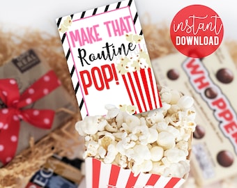 May include: A red and white striped popcorn box filled with popcorn. A pink and black striped card with the text "Make That Routine POP!" is on top of the popcorn.