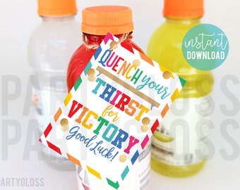 May include: A colorful tag with the text "Quench your thirst for victory! Good luck!" attached to a red sports drink bottle. The tag has a rainbow pattern and gold glitter accents.