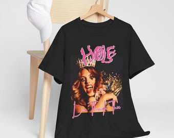 May include: Black t-shirt featuring a graphic of a woman wearing a crown, with the band name "HOLE" in pink, and the text "Live Through This". The shirt is hanging on a wooden hanger.