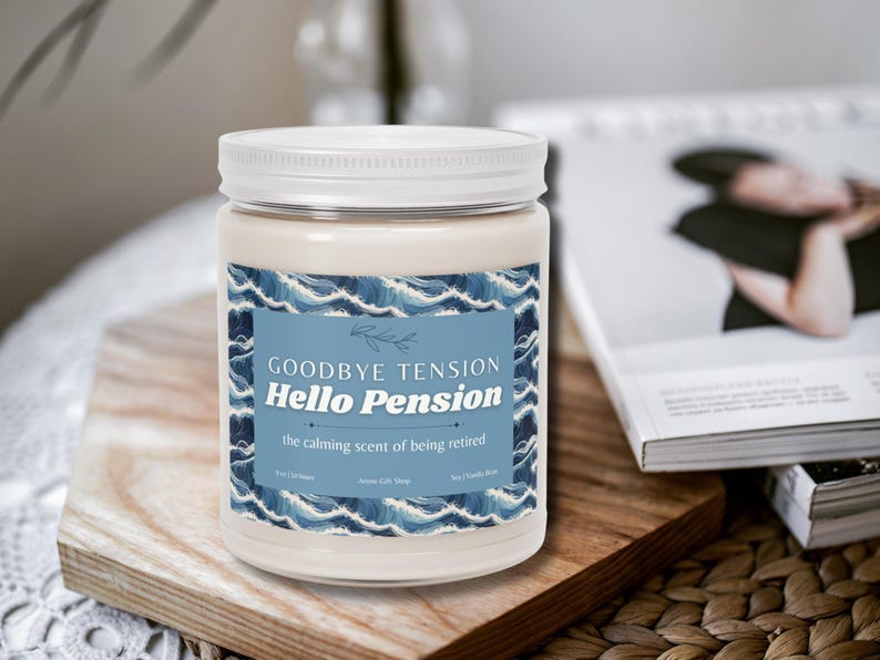 May include: A white jar candle with a white lid, featuring a blue label with the text "Goodbye Tension Hello Pension" and "the calming scent of being retired." The candle sits on a wooden board.