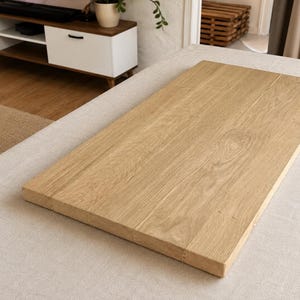 Peut inclure: Une table en bois rectangulaire de couleur claire, avec le grain du bois visible. La table est en bois massif et semble inachevée. Les bords sont nets et carrés. Le bois a une teinte naturelle et chaleureuse.