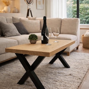 Peut inclure: Table basse rectangulaire en bois clair avec pieds en métal noir en forme de X. Une bouteille de vin, deux verres à vin et une petite plante en pot sont posés sur la table. Le tapis est clair.