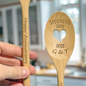 Könnte beinhalten: Zwei Holzlöffel mit einem Herz-Ausschnitt und graviertem Text. Ein Löffel sagt "Spooning Since 2022 G & T" und der andere sagt "Happy Anniversary".