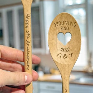 May include: Two wooden spoons with a heart-shaped cutout. One spoon is engraved with "Spooning Since 2022 G & T" and the other spoon is engraved with "Happy 5th Anniversary".