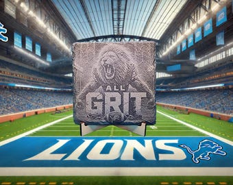 May include: A gray stone plaque featuring a roaring lion with the words "ALL GRIT" and a football. The plaque is displayed on a white stand, set against a football stadium backdrop with the Detroit Lions logo.