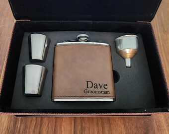 May include: A brown leather-wrapped flask with a stainless steel lid and a silver funnel. The flask is engraved with the name "Dave" and the word "Groomsman". The flask is in a black box with two silver shot glasses.