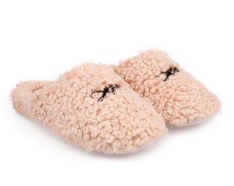 May include: A pair of light brown fuzzy slippers with a black bow detail on each slipper.