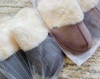May include: Two pairs of fuzzy slippers in gray and brown, packaged in white tulle bags. The slippers have a faux fur trim around the top.