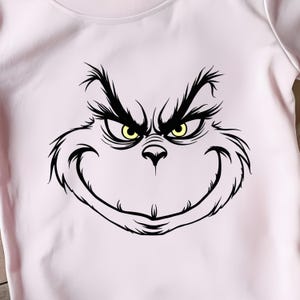 Pode incluir: Uma ilustra&ccedil;&atilde;o em preto e branco do rosto do Grinch com um sorriso malicioso e olhos amarelos. A imagem est&aacute; sobre um fundo rosa.