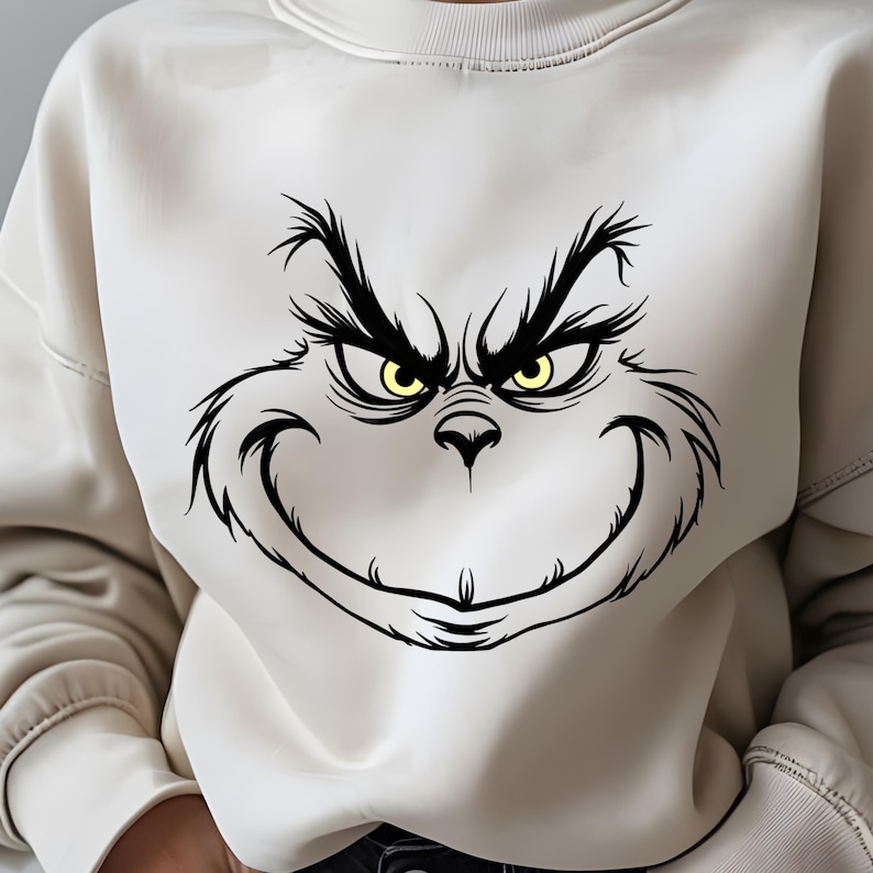 Pode incluir: Uma camisa de moletom branca com uma ilustra&ccedil;&atilde;o em preto e branco do rosto do Grinch. O Grinch tem um sorriso travesso e olhos amarelos.