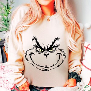 Pode incluir: Uma camisa de moletom branca com uma ilustra&ccedil;&atilde;o em preto e branco do rosto do Grinch na frente.