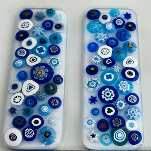 May include: Two rectangular glass pieces decorated with blue and white millefiori designs. The designs include various floral and geometric patterns in shades of blue, white, and clear glass. The pieces are set against a white background.
